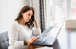 © Louis-Paul Photo - Senior woman at home kitchen table feeling stressed and confused while looking at multiple bills working on her laptop