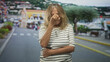 © Krakenimages.com - Senior woman pinches nose and clutches abdomen on a seaside town street, eyes closed and posture hunched; disgust.