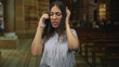 © Krakenimages.com - Hispanic young brunette woman holding smartphone to ear and gesturing with open hand in church building, mouth open as she speaks loudly to caller; frustration distraction.