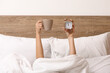 © Pixel-Shot - Female hands with alarm clock and cup of coffee in bed at home