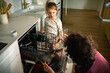 © Davor - Parent teaching child to load dishwasher in modern kitchen