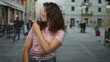© Krakenimages.com - Woman with striped shirt points finger to the right, smiling and showing forearm on a busy street near cafe tables; playful curiosity.