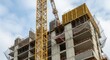 © twilight mist - Tall yellow construction crane stands next to a multi-story building under development.