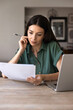 © fizkes - Focused adult woman sits at desk, reading documents text, analyzing details, reviewing information of contract terms data, learning insurance papers, doing remote work from home office, vertical shot