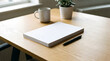 © AiStock B - Minimalist Workspace Mockup with Blank White Book, Pen, Coffee Mug, and Potted Plant on Wooden Desk in Bright Sunlit Room
