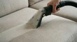 © evgeniya - Hand steam cleaning light beige fabric sofa with vacuum machine, visible clean line, home, cleanliness, hygiene, maintenance.