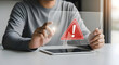 © Aklima - Man sitting at table interacting with tablet and warning sign appears