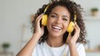 © Volha - Happy young African American woman with curly hair listening to music on yellow headphones indoors