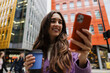 © Westend61 - Smiling woman holding coffee and smartphone outdoors in urban city