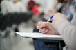 © slexp880 - Person taking notes at a desk in a classroom or lecture hall. Close-up view of hands writing a test or essay with blurred background. Education and professional training. Photo