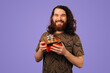 © Vulp - Caucasian Man Holding Wrapped Gift Box, Bearded Smiling Presenter In Patterned Shirt Against Purple Studio