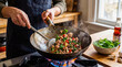 © Mary - Man cooking flavorful Thai basil pork (Pad Krapow) in a smoking wok on a gas stove in a home kitchen.