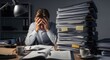 © Chenda - A stressed man sits at a desk, overwhelmed by a large stack of papers. He has his head in his hands, displaying a look of frustration and exhaustion. The desk is cluttered with a lamp, pens, a mug