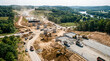 © Celt Studio - drone view major highway overpass construction site heavy machinery concrete pillars building new road bridge infrastructure expansion project beautiful green forest river landscape