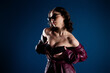 © deagreez - Young woman in sunglasses and burgundy leather coat posing sensually in dramatic studio lighting, fashion portrait with a moody blue background and confident, glamorous attitude