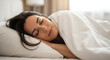 © LAB IMAGE - A serene young woman with dark hair is sleeping soundly and peacefully in a comfortable white bed, resting her head on a soft pillow under a cozy duvet.