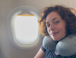 © Юлия Завалишина - Rest on plane. Young woman napping sitting by porthole in business jet using neck pillow for travel. Passenger girl flying in plane. Girl sleeping in airplane going on trip vacation. Traveling girl