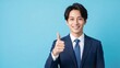 © YT - ブルー背景で親指を立てて微笑む日本人ビジネスマンのポートレート。信頼感と好印象を伝える、成功、承認、推薦、サポート、採用、営業、サービス案内、企業広告向けの人物素材