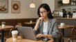 © Cloudyew - Focused Young Woman Working on Laptop in Cozy Café Setting