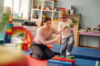 © standret - Female caregiver assisting young boy with balance on colorful blocks in a bright playroom filled with educational toys and soft mats for children