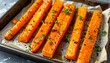 © Yana Perelotova - Glossy roasted carrot sticks on baking tray with herbs and spices, healthy homemade vegetable side dish in warm natural light.