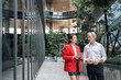 © chokniti - Office conversation business people modern building urban walkway professional meeting red jacket white shirt glass facade outdoor office corporate discussion