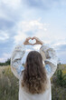 © Anna - Young Ukrainian woman in an embroidered shirt holds a heart made of hands above her. National identity, love for the homeland, Independence Day. Stop the war. Hope and faith. Back view