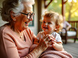 © Igor - Grandmother holding laughing toddler girl on home porch.