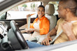 © Anastasiya - Smiling young Black woman fastening seatbelt in car while man sits in driver seat, couple preparing for road trip, safety and travel lifestyle concept