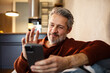 © Davor - Smiling middle-aged man waving on smartphone video call at home