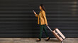 © Home-stock - Young caucasian female traveler walking with rolling suitcase while looking at phone