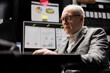 © DC Studio - Old business manager executive sitting at office desk before consulting meeting, inspecting quarterly company results analysis data paperwork on laptop. Bureaucratic workplace filled with flowcharts