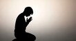 © koji antero - Silhouette of person kneeling in prayer, hands clasped, against soft light background.