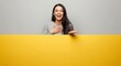 © Ariestia - Young woman smiles while presenting a blank yellow banner with her hand.