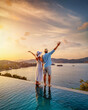 © moofushi - A happy couple on summer vacation standing by the swimming pool enjoys a beautiful sunset behind the sea