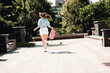 © deagreez - Young woman in casual summer outfit runs through a sunny park in the city carrying a pink backpack capturing a joyful outdoor moment of urban life and carefree style