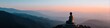 © Andrii Zastrozhnov - Back view of meditative buddha statue overlooking expansive layered mountain panorama at sunrise with soft pink and blue hues