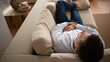 © olga_demina - A man lies on a couch holding his stomach, looking unwell in a modern living room with a wooden coffee table and beige rug.