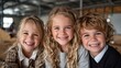 © svastix - Three happy children with curly hair and bright smiles pose closely together, capturing the warmth and joy of childhood in a lively classroom environment filled with laughter.