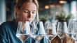 © DP - Female wine taster examines multiple wine glasses filled with clear liquid, seated at a table in a modern restaurant with soft lighting and decorative plants in the background