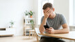 © Konstantin - Upset man covering his face in despair while reading a message on his smartphone. Frustrated person receiving bad news at home. Stress and anxiety concept with copy space for text