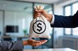 © Netsai - A close-up shot of two people exchanging a white cloth money bag with a prominent dollar sign, symbolizing a financial transaction or payment.