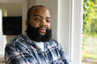 © Wavebreak Media - Adult African American man posing at home by white window wearing plaid shirt daylight bathing face