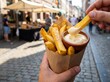 © wahid - Person eating a cone of traditional Belgian fries with mayonnaise on a city street.