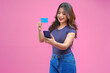 © ChristyMerry - Happy successful Asian girl holding her smartphone and credit cards over isolated pink background.
