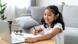 © slametamirin - Young girl engaging in online learning at home with laptop.