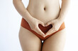© Mykola - Close-Up of a Woman's Hands Making a Heart Shape Over Her Abdomen in Brown Underwear on White Background