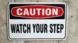 © Norah Allen - Rectangular caution sign with red and white text CAUTION above black text WATCH YOUR STEP against concrete warning danger safety hazard attention alert notice lettering message