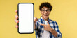 © Maryna - Excited man points to blank smartphone screen. Guy shows mobile phone display with copy space for app ad. Positive teen promotes new tech on yellow background.