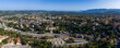 © Aerial Film Studio - Aerial view of Grasse, France, with terracotta roofs, terraced housing, winding roads, and a central junction. The Prealps form an undulating backdrop in bright light.